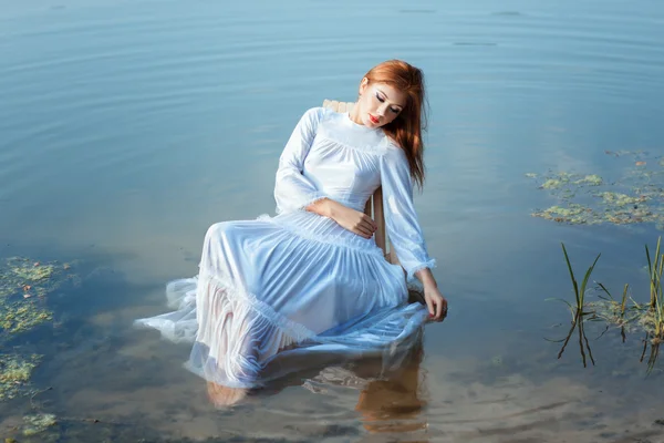 Girl white dress sitting on chair in a lake.