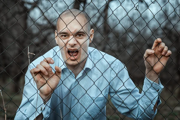 Angry and fearful man grinning over the fence mesh.
