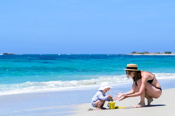 Adorable mother and little daughter building sandcastles at tropical beach