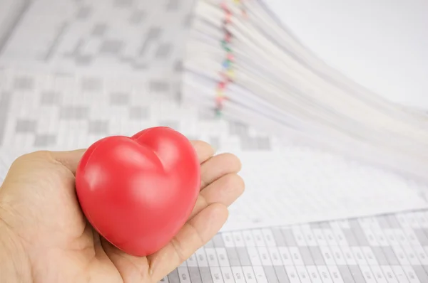 Red heart in hand have blur pile paperwork as background