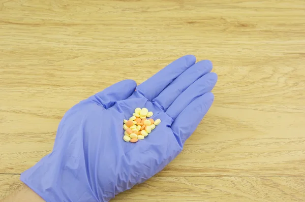 Hand wear purple latex glove holding yellow and orange pills