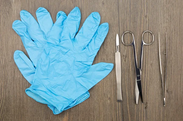 Silver scalpel surgical scissors and forceps beside blue latex glove