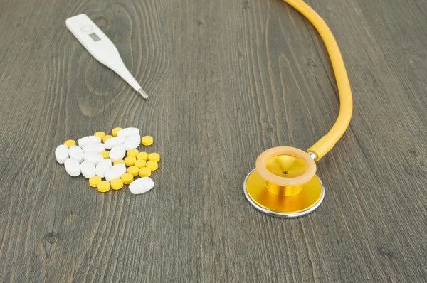 Gold stethoscope and pile of pills with digital thermometer