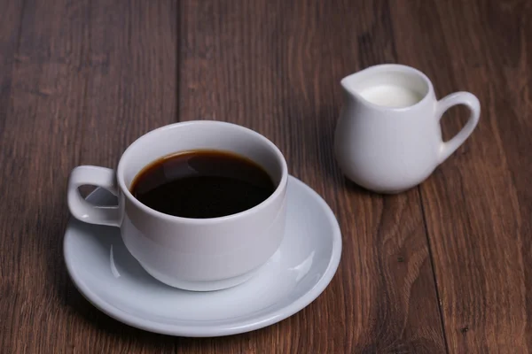 Mug with black coffee and milk jug on the wooden background