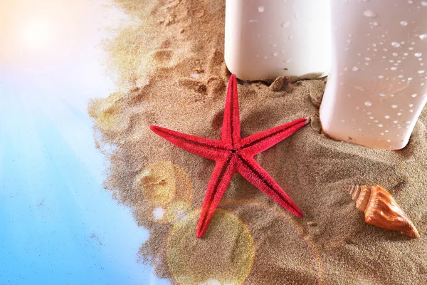 Two sunscreen on sand with starfish and shell on table