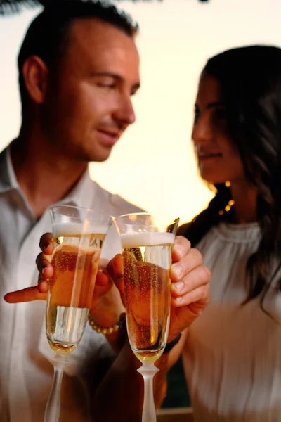 Toast young couple with glasses in the foreground at sunset