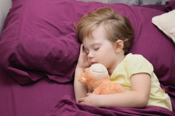 Girl sleeping peacefully with her teddy bear on the bed