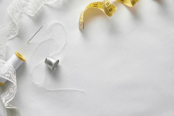 Sewing tools with tape on white fabric background top view