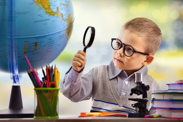 Boy looking through magnifying glass at globe