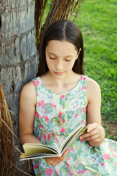 Cute teen girl reading book sitting on green grass