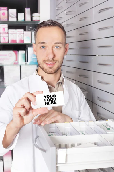 Young pharmacist at medicine cabinet holding box with copyspace