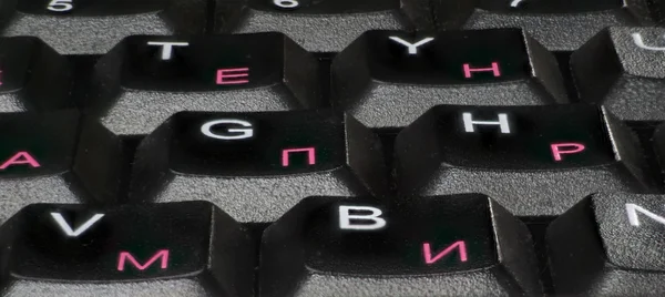 Closeup of a black computer keyboard, English and Russian letters.