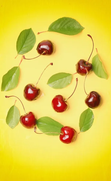 Sweet cherries with leaves on a yellow wooden background flat top view over head cover for the cookbook