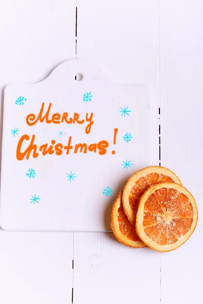 New Year background cutting board with the words Merry Christmas and with dried oranges on a white wooden view from above greeting Winter brochures, postcards, magazines