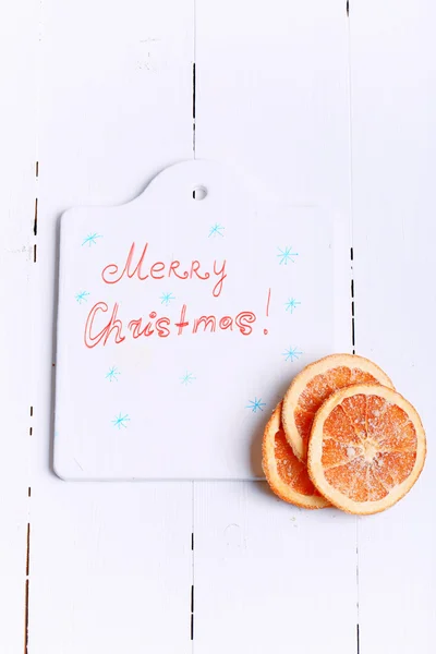 New Year background cutting board with the words Merry Christmas and with dried oranges on a white wooden view from above greeting Winter brochures, postcards, magazines