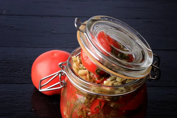Canned pickled tomatoes in a glass jar on a black wooden background rustic style