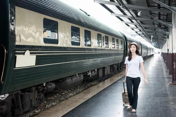 Young Asian tourist with luggage waiting train in station.