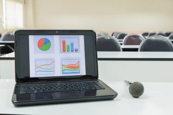 Laptop and microphone in front of empty chairs at classroom