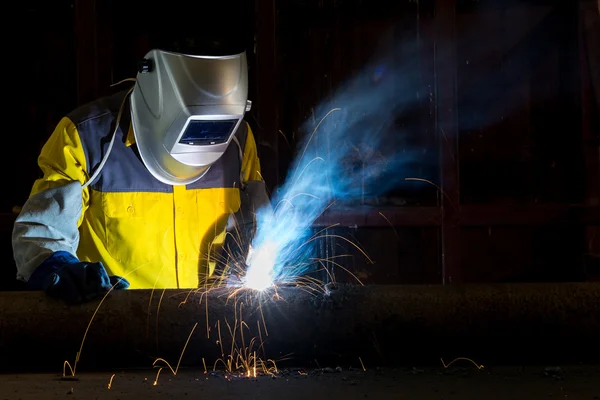 Worker with protective mask welding metal in factory