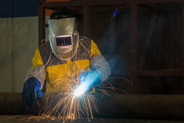 Worker with protective mask welding metal in factory