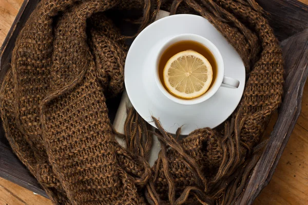 Cup of hot tea with lemon on brown wooden tabletop with warm winter scarf and book, selective focus