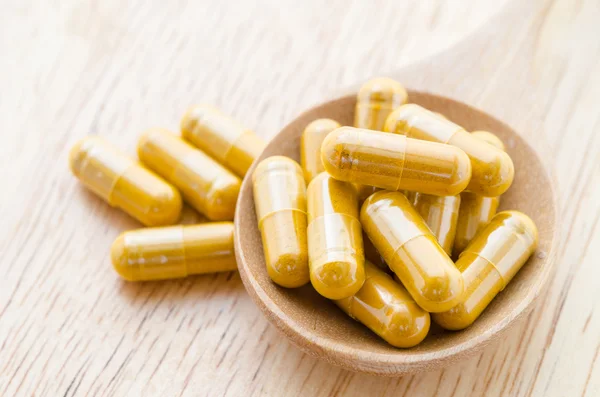 Vitamin capsules in a wooden spoon.
