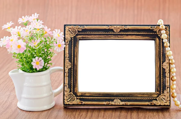 Flowers vase and vintage picture frame on wooden desktop.