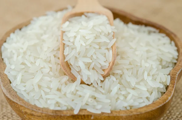 Raw rice and wooden spoon in wooden bowl.