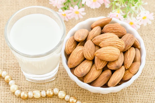 Almond milk in glass and almonds in white cup.