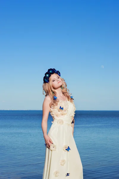 Girl near the sea in a white dress and wreath