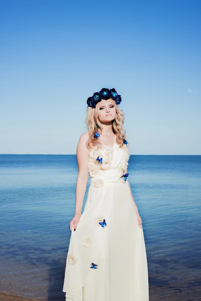 Girl near the sea in a white dress and wreath