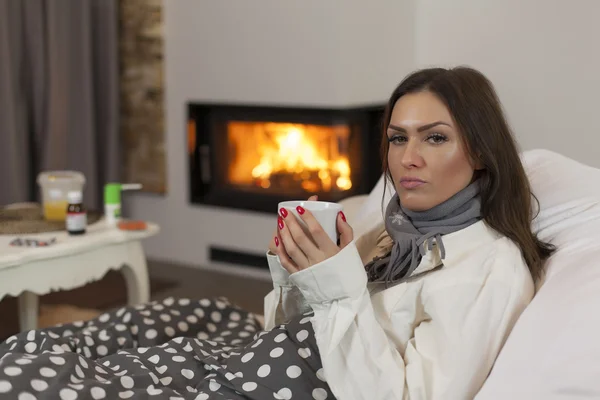 Sick young woman in bed drinking hot tea