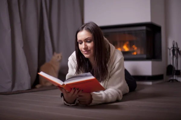 Beautiful woman lying on floor and reading book by fireplace