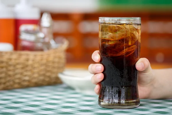 Hand holding glass of cola drink on table