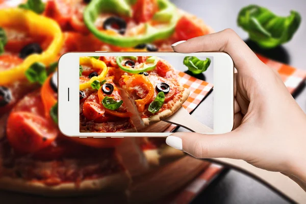 Woman photographing on smartphone, vegetarian pizza
