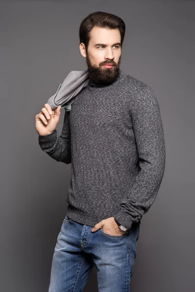 Young man with a beard, wearing a jacket and jeans standing