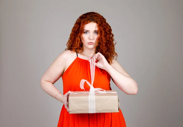 Beautiful fat girl with red hair with a gift box in hand on gray background