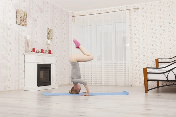 Beautiful blonde woman practicing yoga stretching at home with blue mat in gray bodysuit, pink socks. Stand on arms and hands