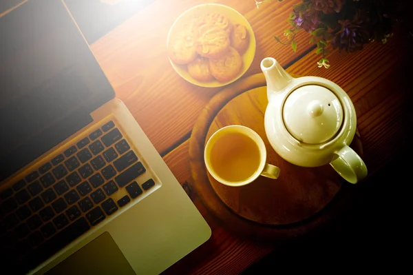 Cup, tea pot ,cookies and laptop on wooden desk