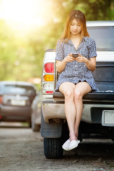 Beautiful young woman using her mobile phone sit on car