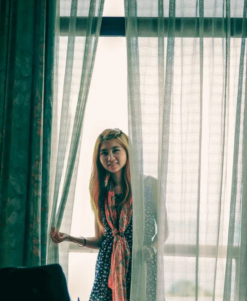 Asia young girl holding white curtain near window