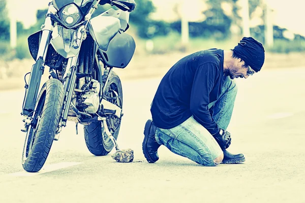 Motorcycle parked in country road with Biker    tying his shoes