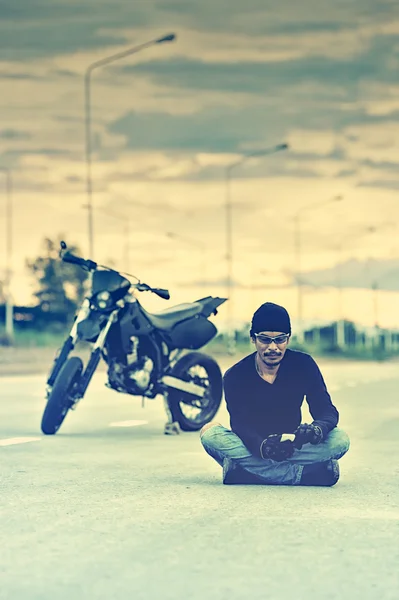 Biker relax sitting with motorbike on road in sunset