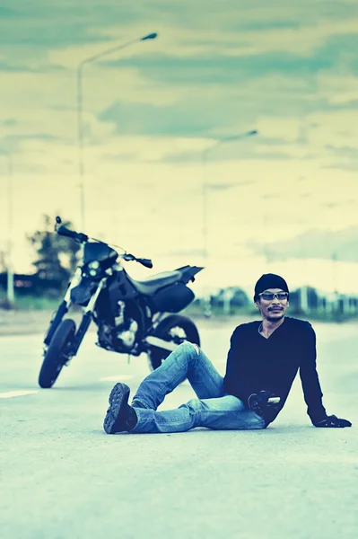 Biker relax sitting with motorbike on road in sunset