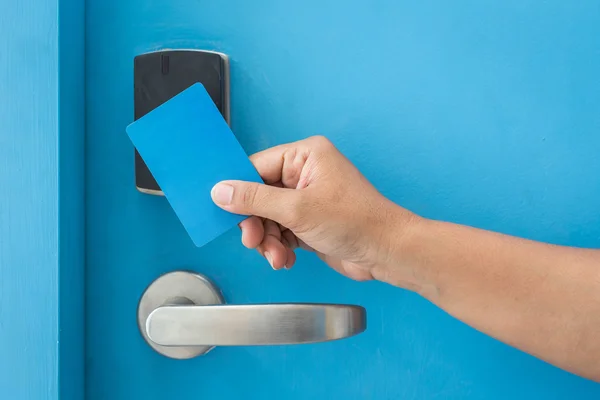 Hand holding blue hotel keycard in front of electric door