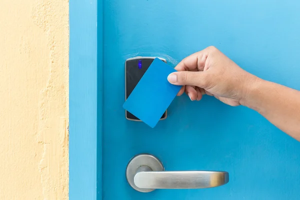 Hand holding blue hotel keycard in front of electric door