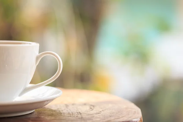 White coffee cup on table in garden with blur light bokeh