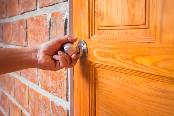 Hand holding metal silver doorknob on wooden door