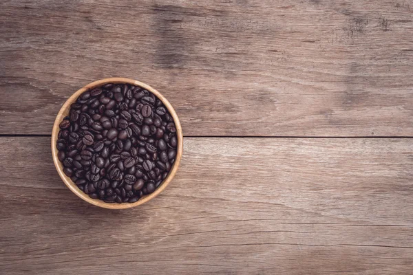 Coffee beans in wooden bowl on wooden table top view