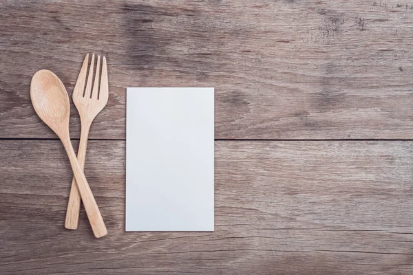 Wooden spoon, fork and blank paper on wooden table top view